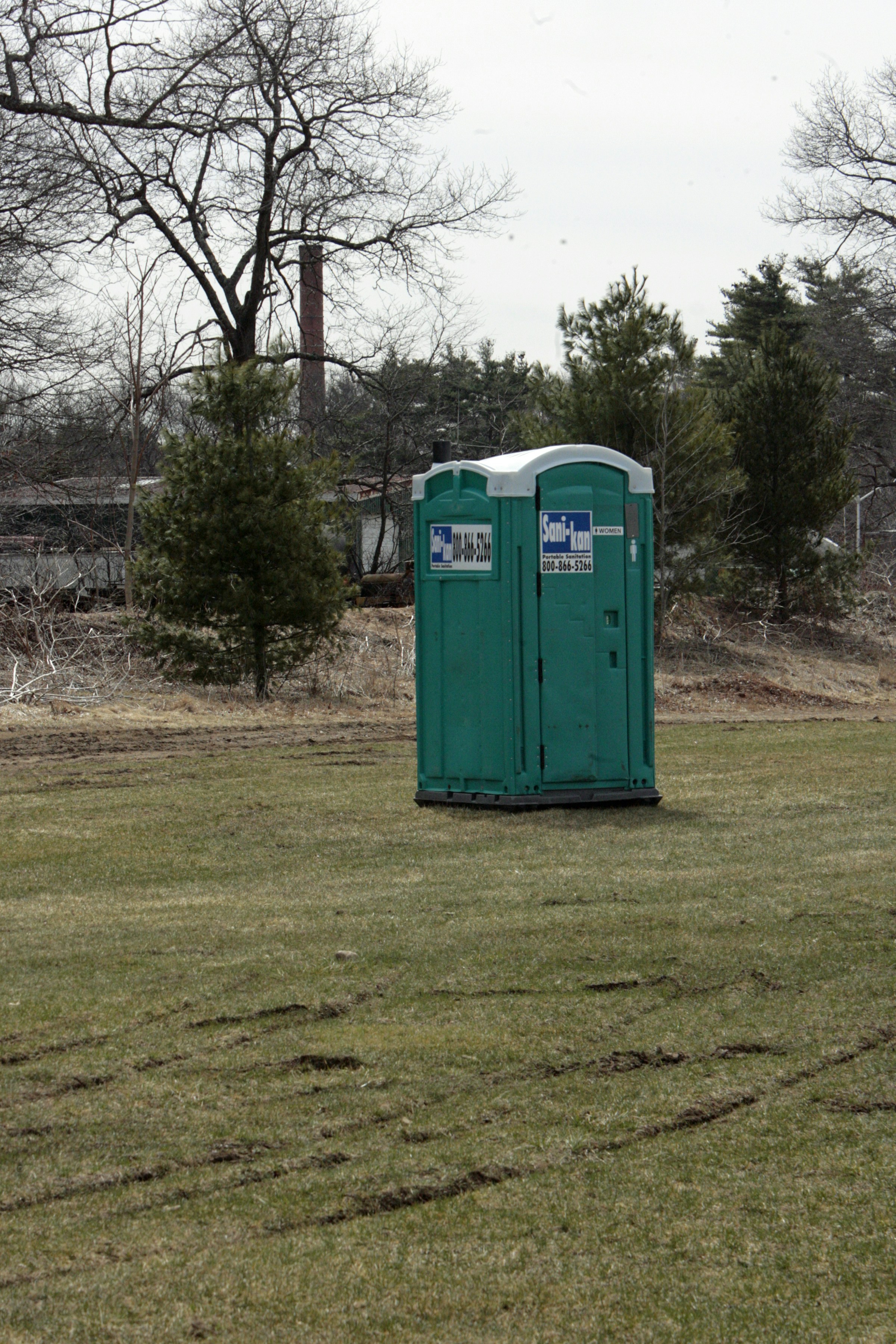 A portable toilet in a field with trees in the background