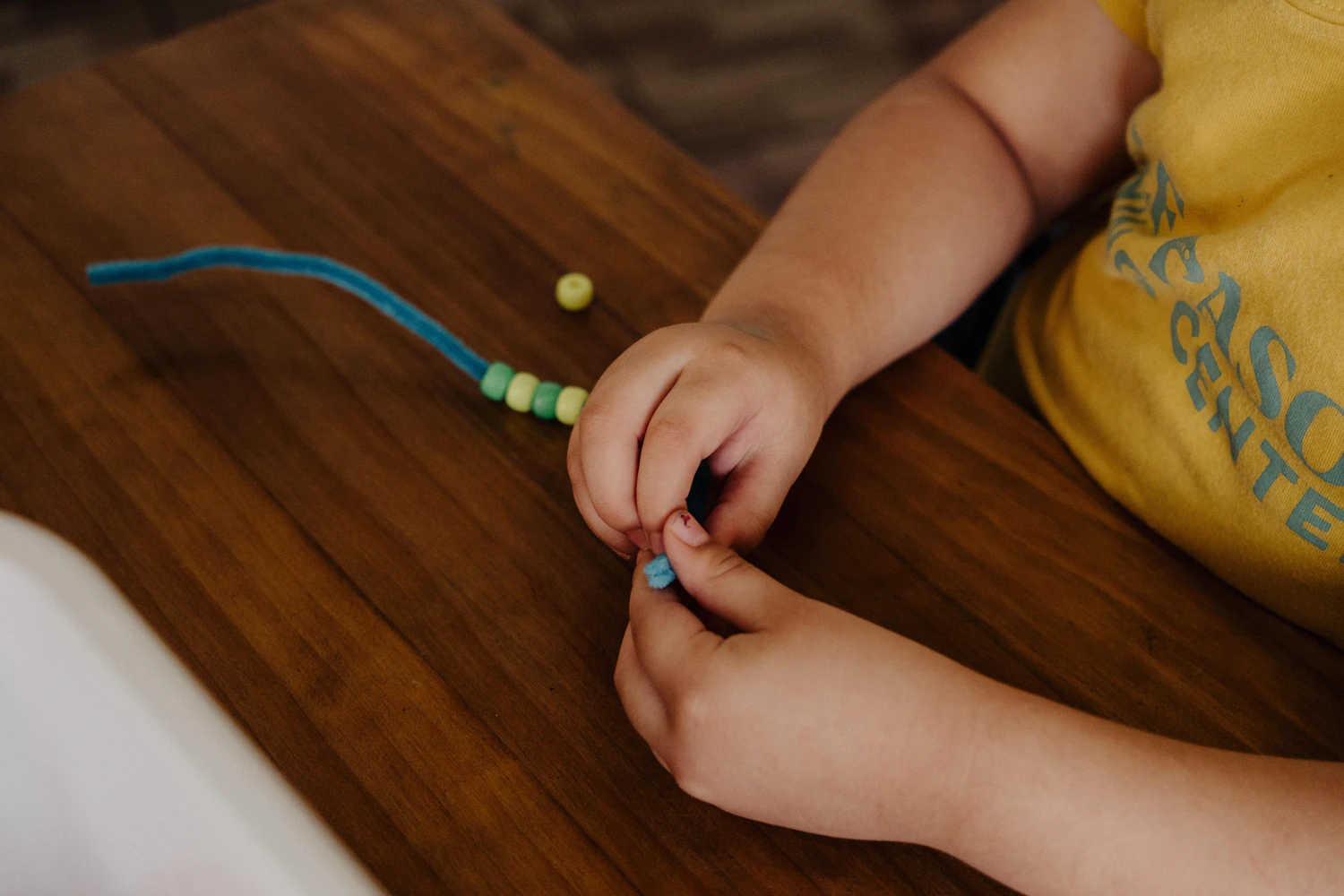 A child's hands moving small beads one at a time on a table