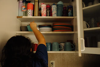 A woman reaching up into a kitchen cabinet