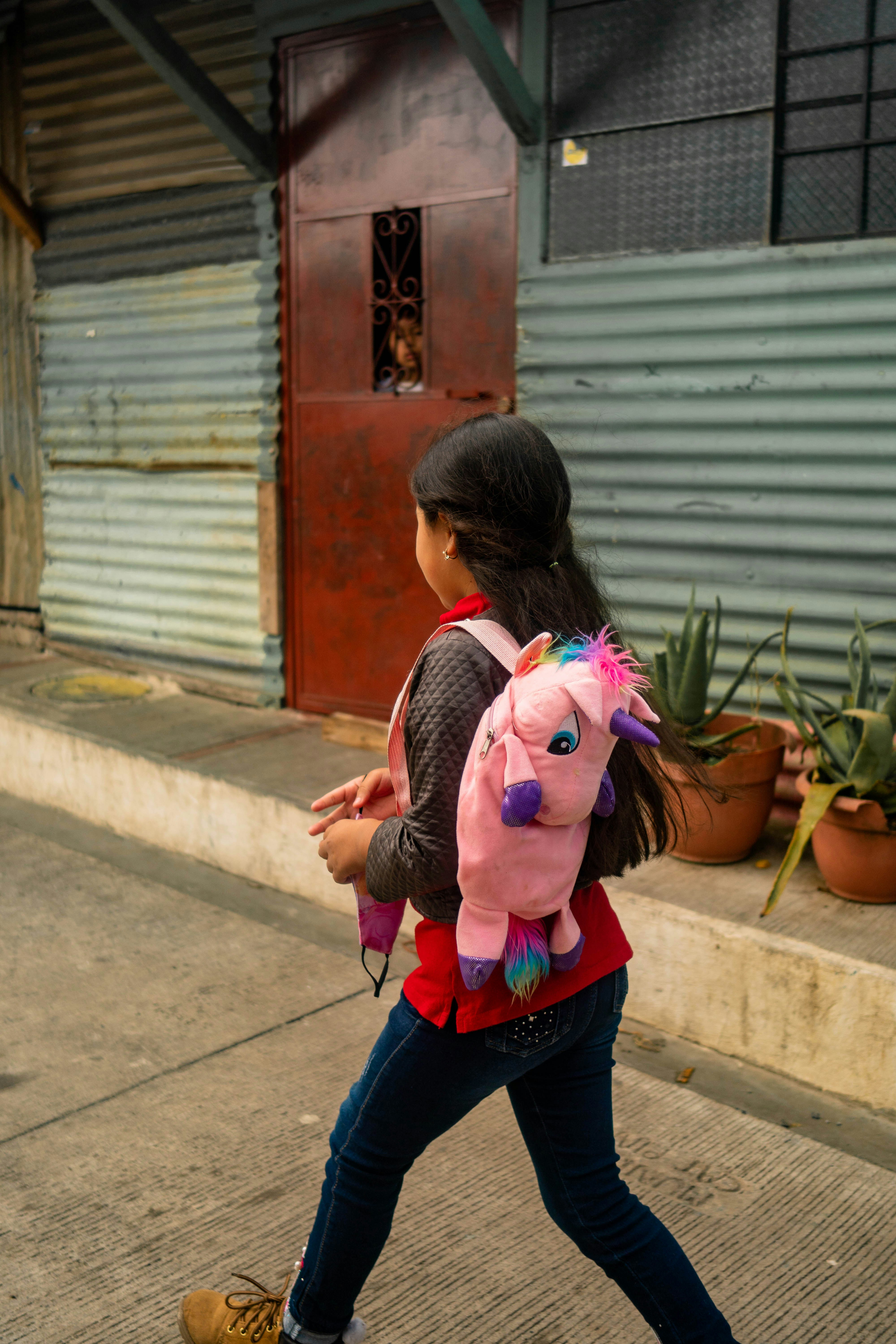 A little girl walking down the street with a pink pony backpack
