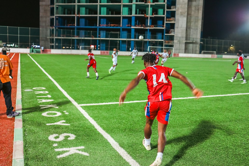 Match de football en soirée sur un terrain synthétique : un joueur en maillot rouge numéro 14 s’apprête à effectuer une touche