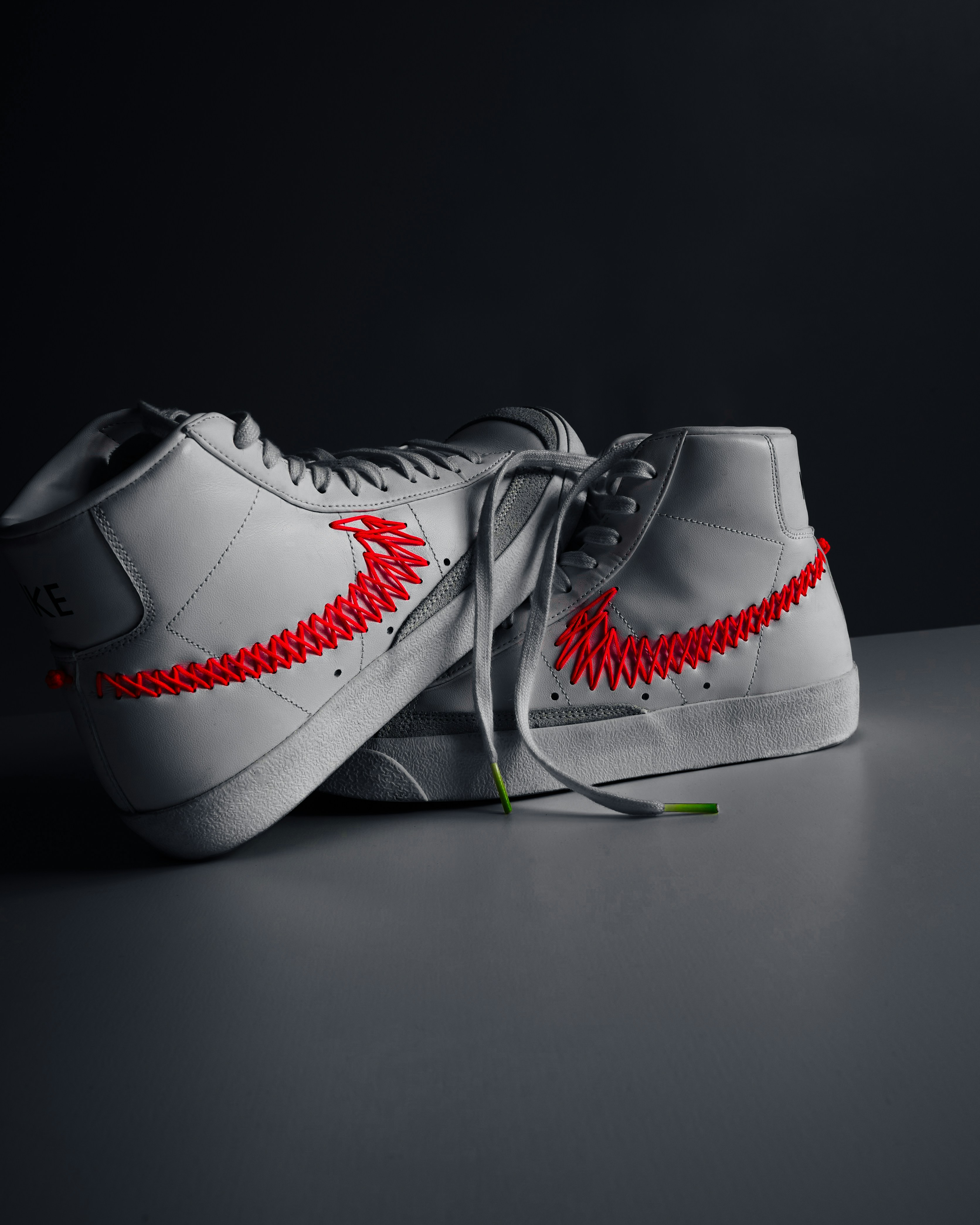 A pair of white sneakers with red stitchs on them