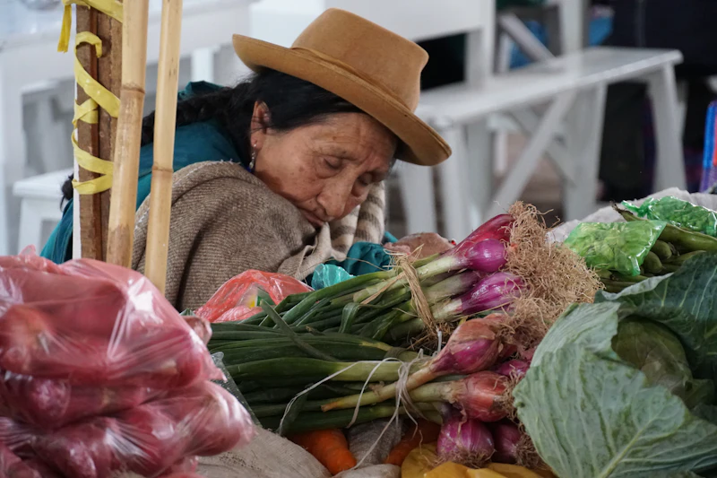 A market vendor behind a table of fresh vegetables in Cusco