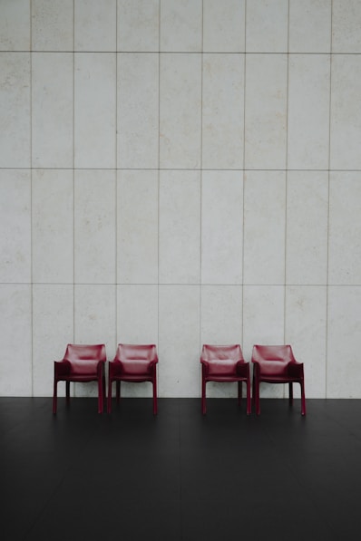 Three red chairs sitting in front of a white wall
