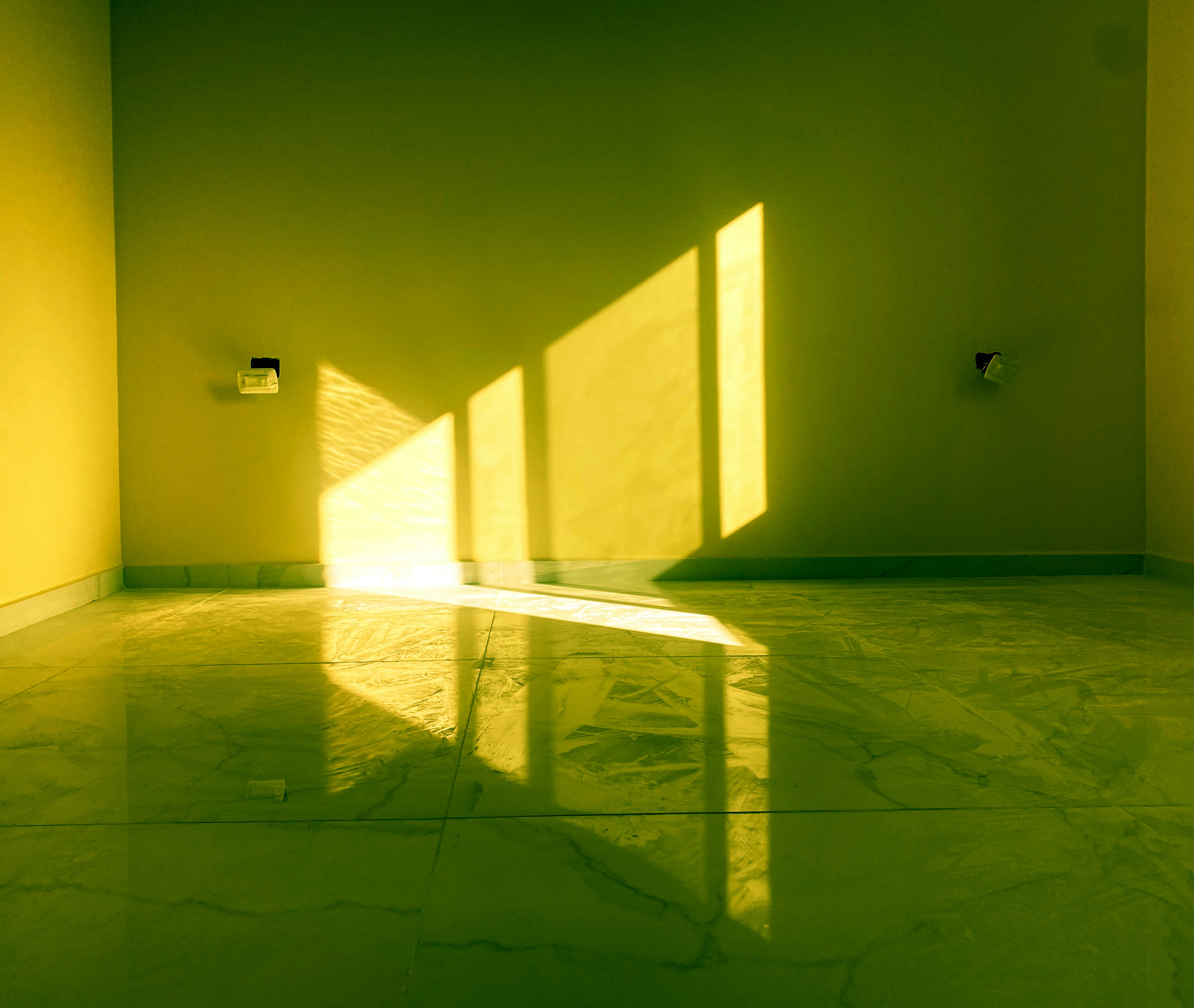 Ein leerer Raum mit gelben Wänden und hellem Sonnenlicht, das durch die Fenster fällt