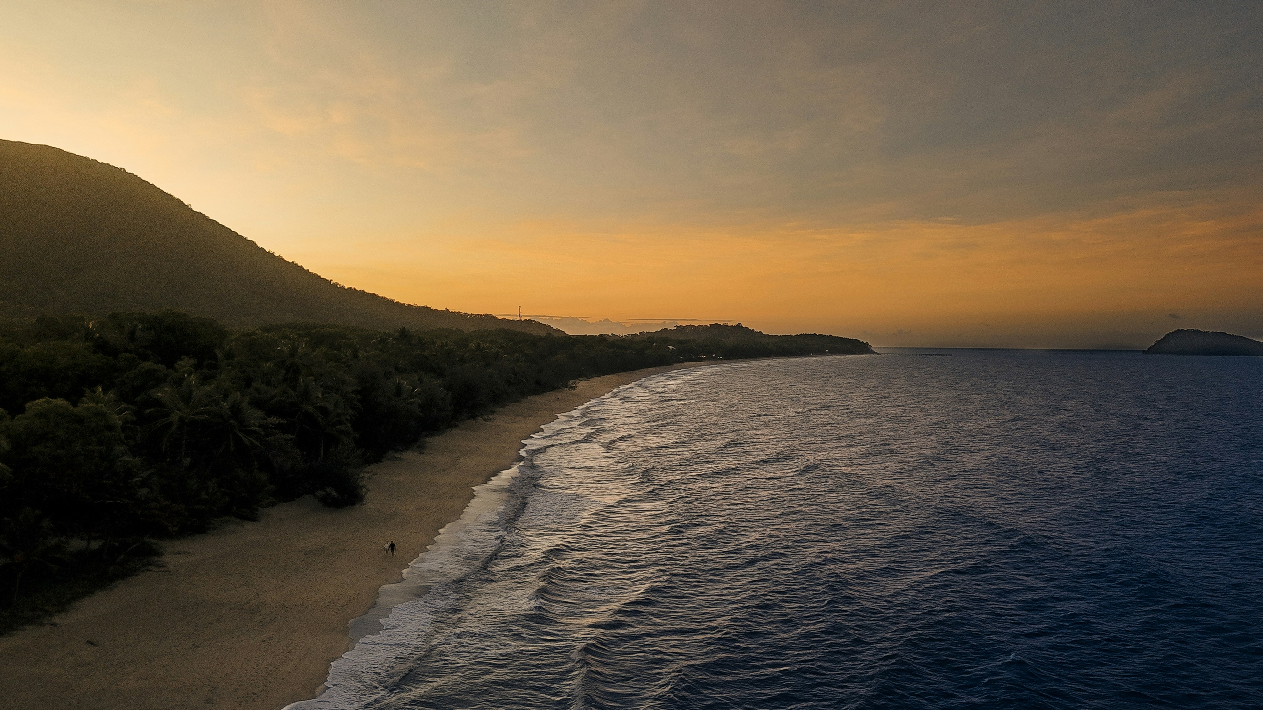 Die Sonne geht über dem Ozean unter, im Hintergrund ein Berg
