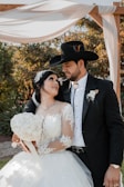 A bride and groom pose for a picture under a wedding arch