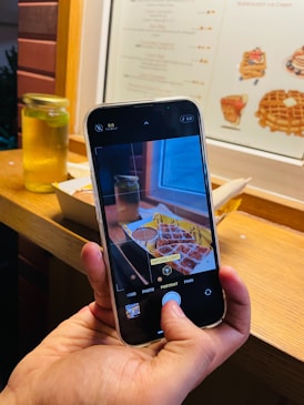 A person holding up a cell phone to take a picture of food
