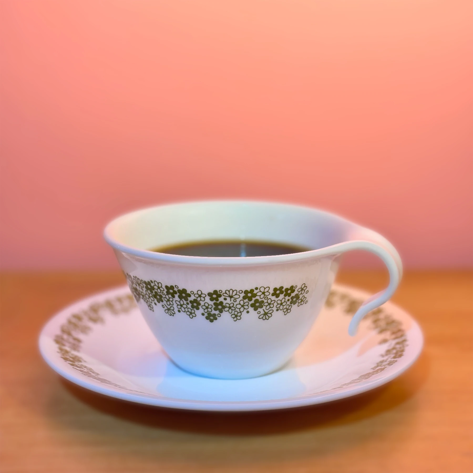 A white cup and saucer banded with small green printed flowers against a pink wall