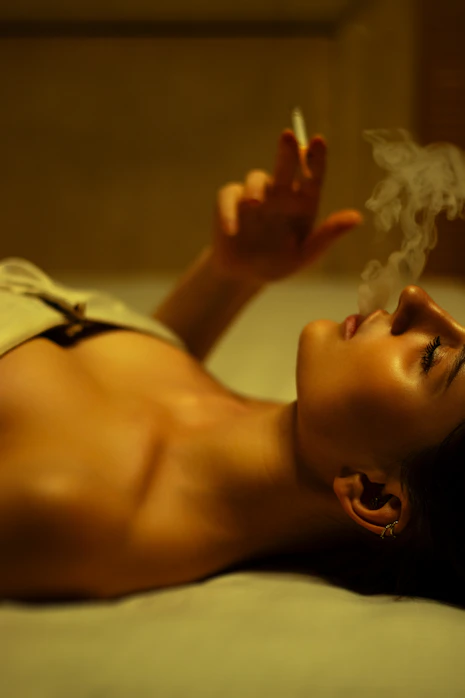 A woman laying on a bed smoking a cigarette
