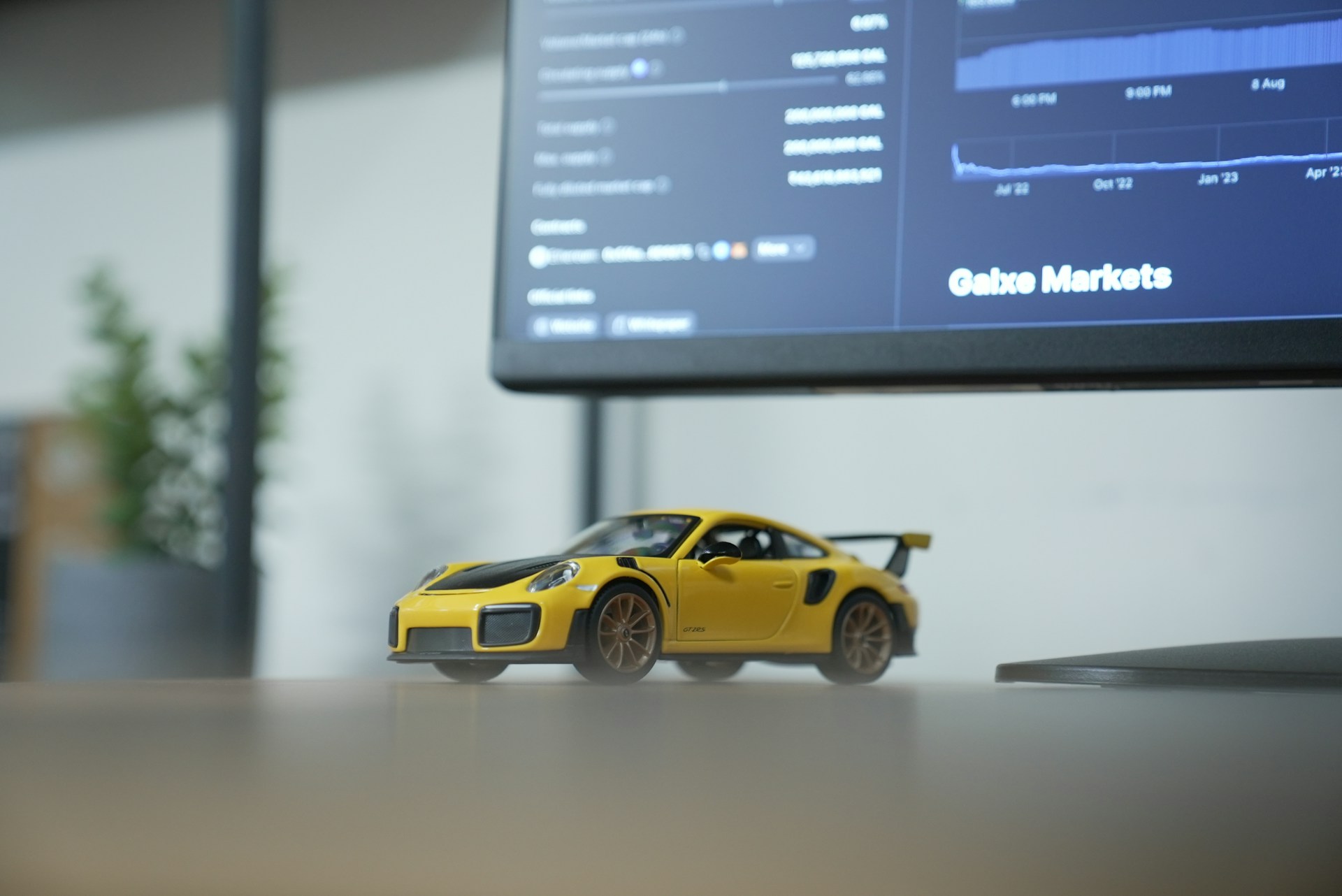 A yellow toy car sitting in front of a monitor