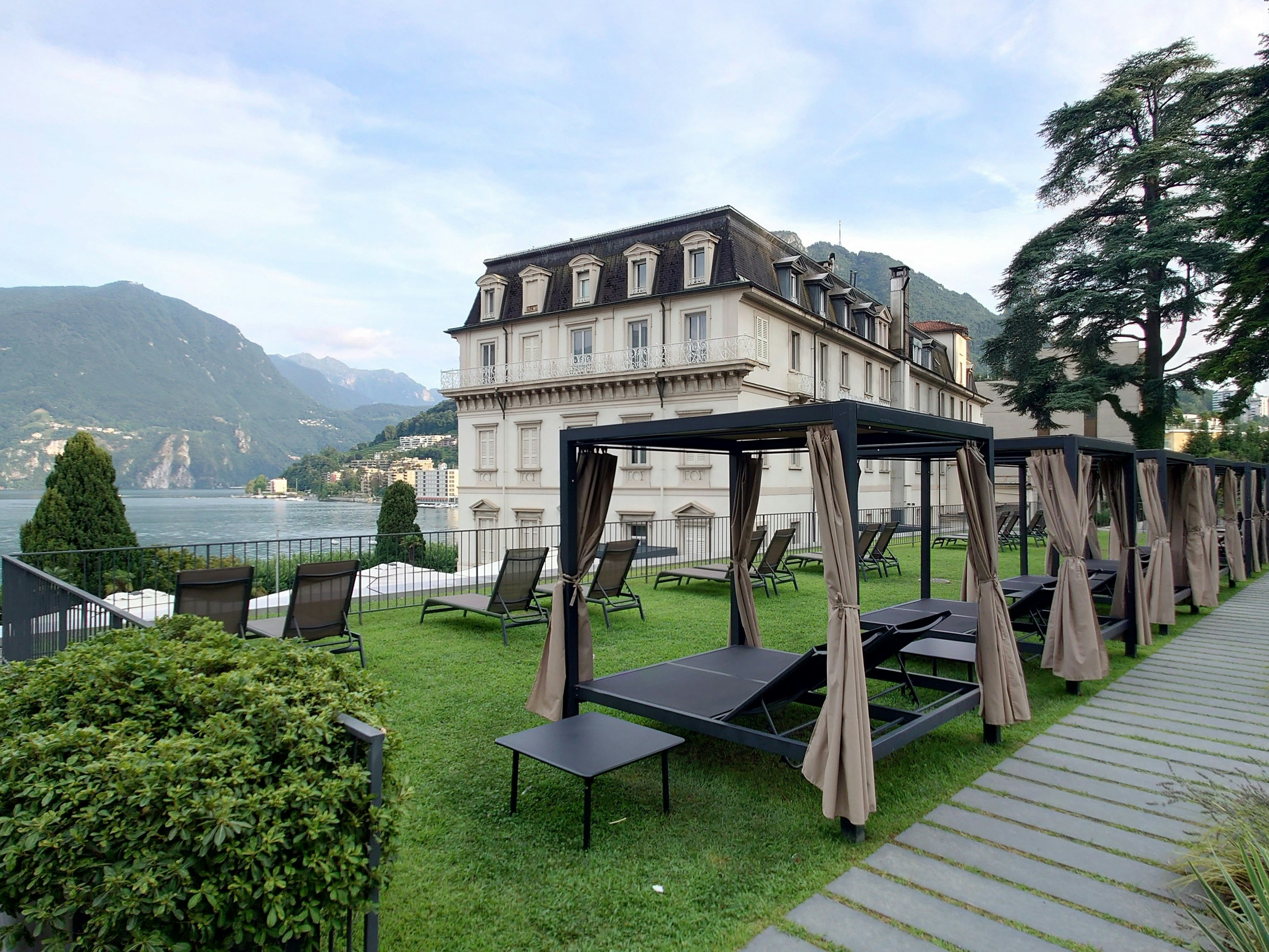 A large building with a lawn and picnic tables in front of it, Sun Deck of Hotel Splendide Royal Lugano overlooking Lake Lugano.