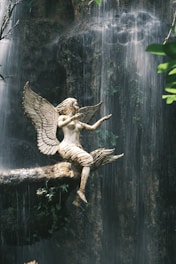 A statue of an angel sitting on a branch in front of a waterfall