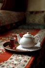 A tea pot and a cup on a tray on a bed
