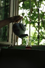 A person pouring tea into a small glass vase