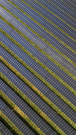 An aerial view of rows of solar panels separated by strips of green grass