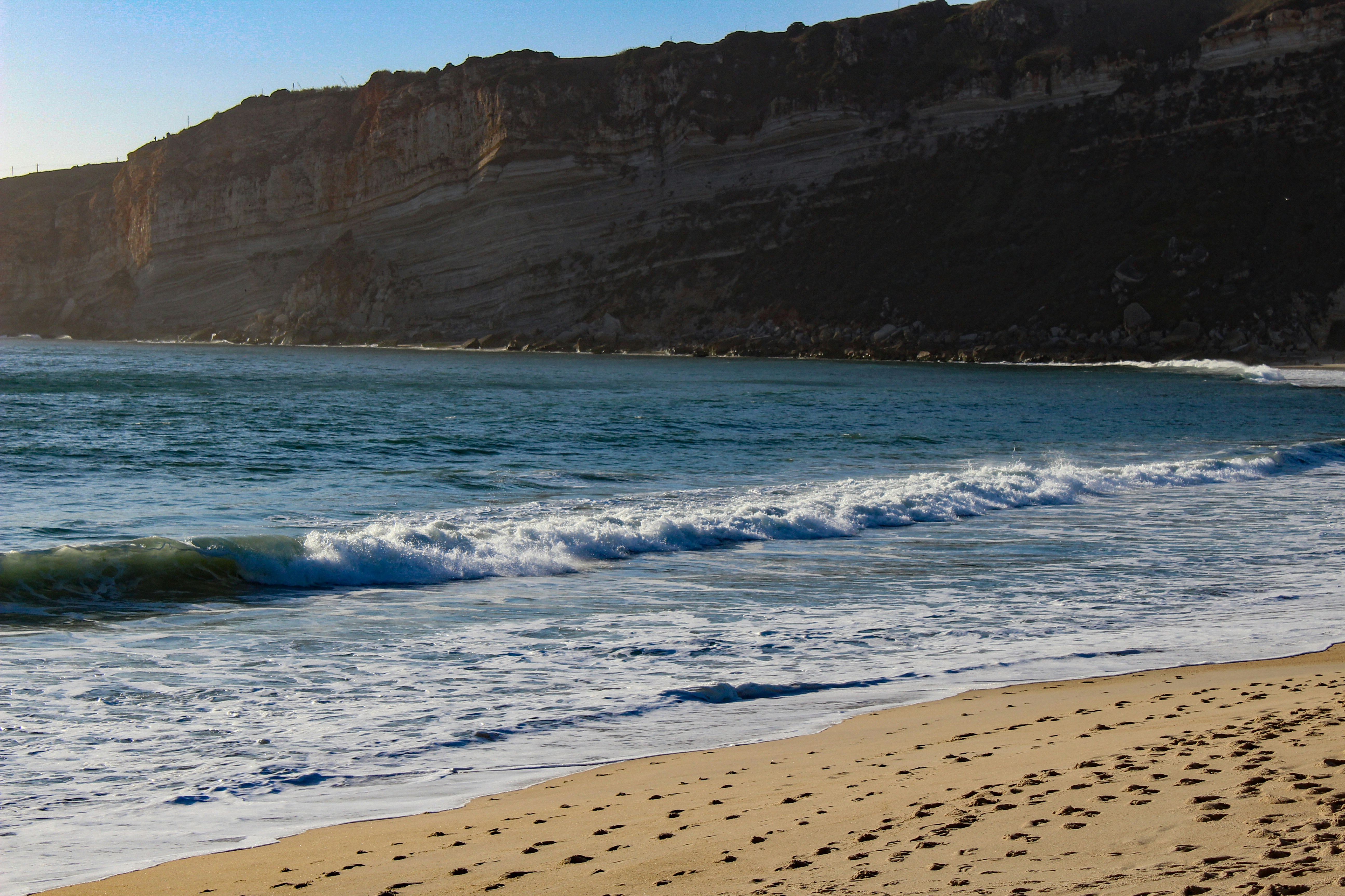 A beach with waves coming in to shore and a cliff in the background