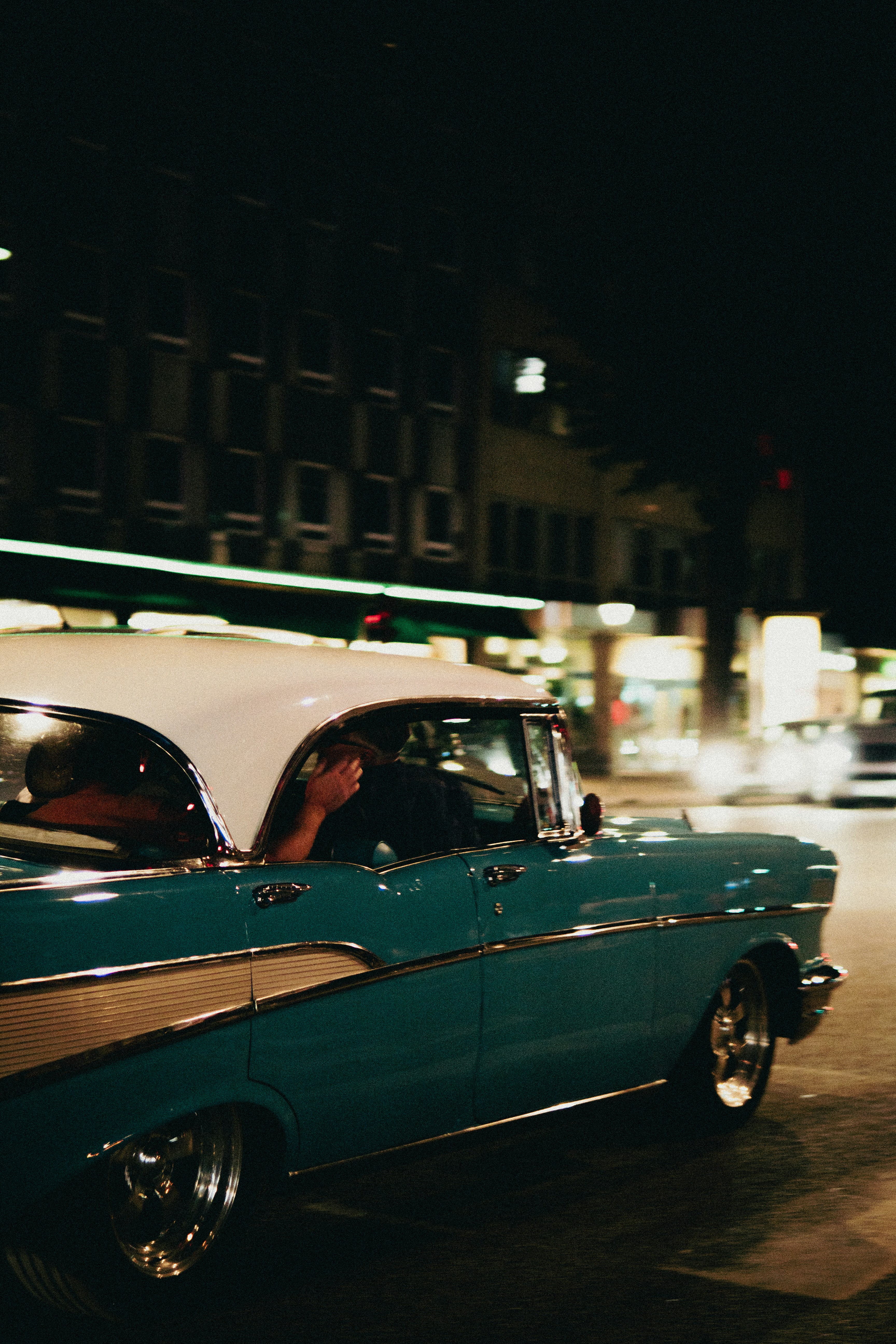 A classic car driving down a street at night