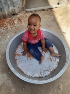 A baby sitting in a metal bowl on the ground