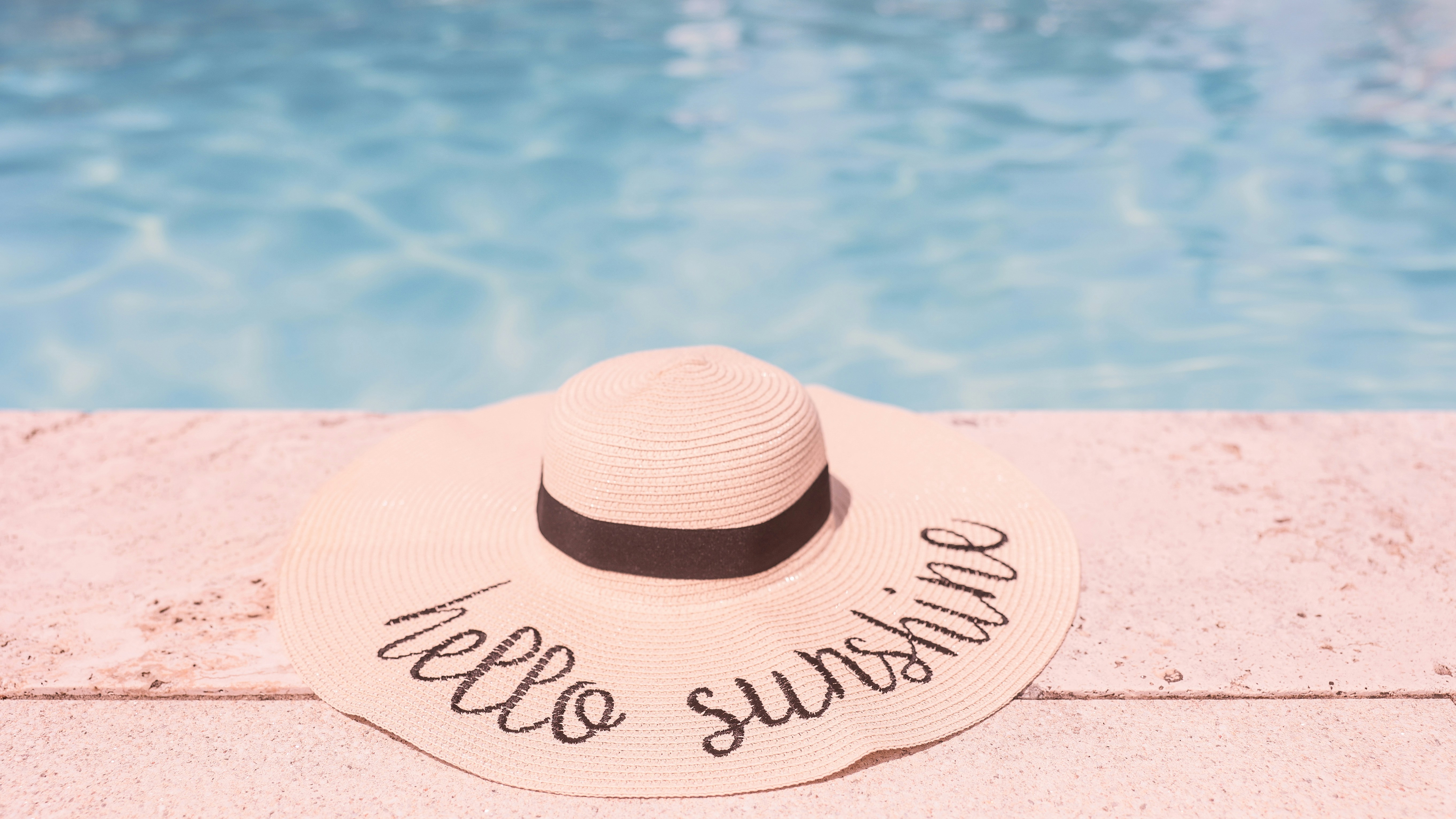 A hat sitting on the edge of a swimming pool, Sunhat by the pool
