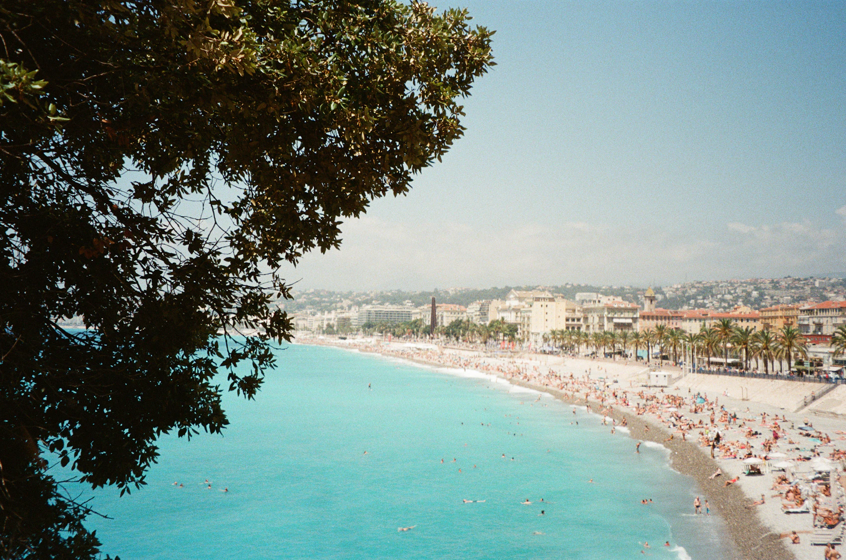 A busy summer day on Nice's pale pebble beach beside turquoise water