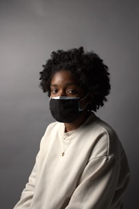 A woman wearing a black face mask and a white sweater