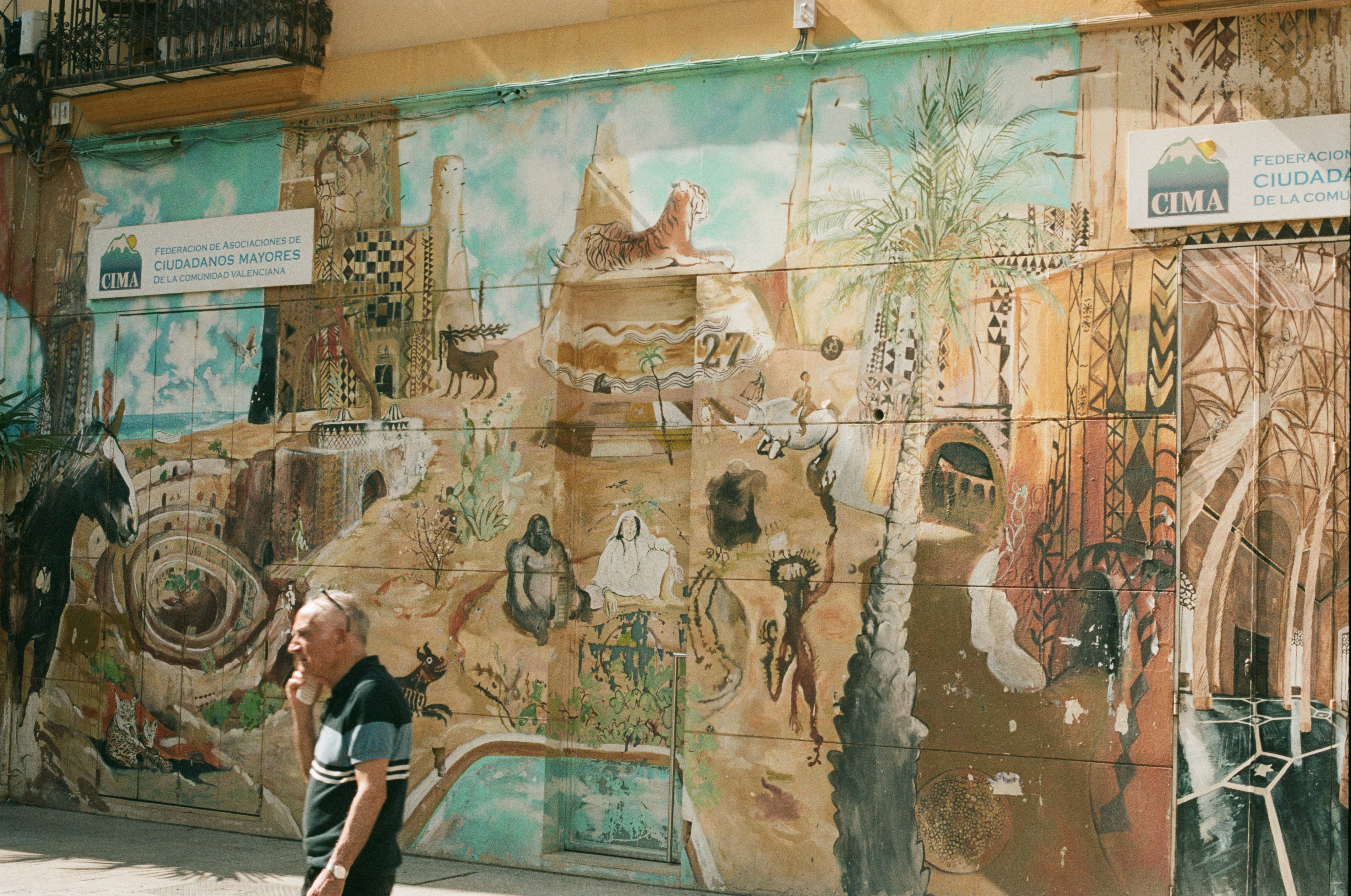 A man walking down a street past a wall covered in murals
