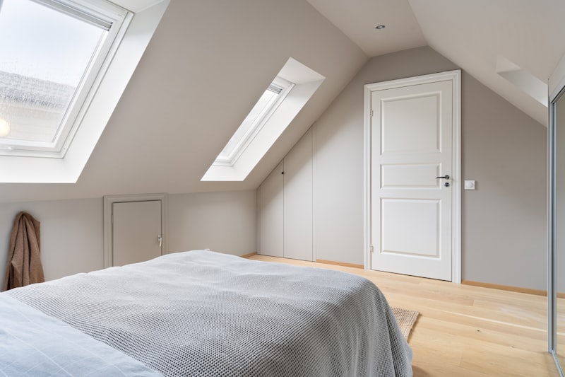 Bright modern loft conversion bedroom with a sloped ceiling, two roof skylights and light wood flooring
