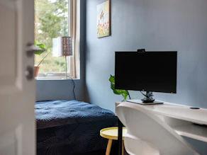 A bedroom with a bed, desk, and computer monitor