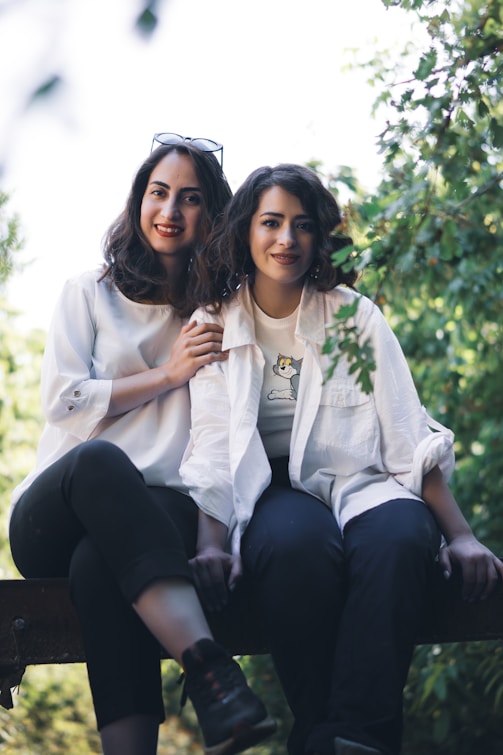 A couple of women sitting on top of a wooden bench