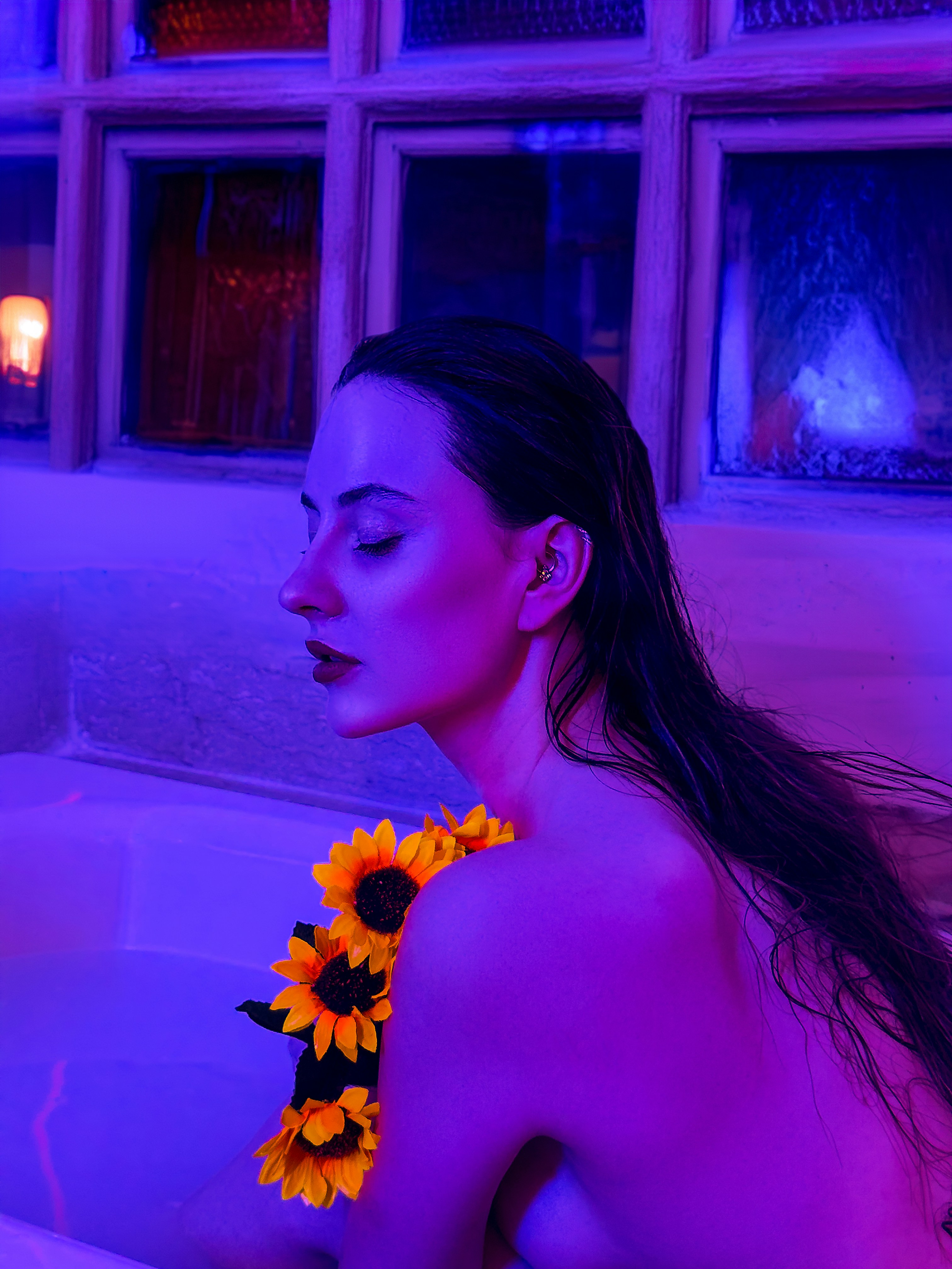 A woman in a hot tub with sunflowers around her neck