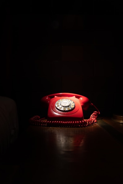 A red telephone sitting on top of a wooden table