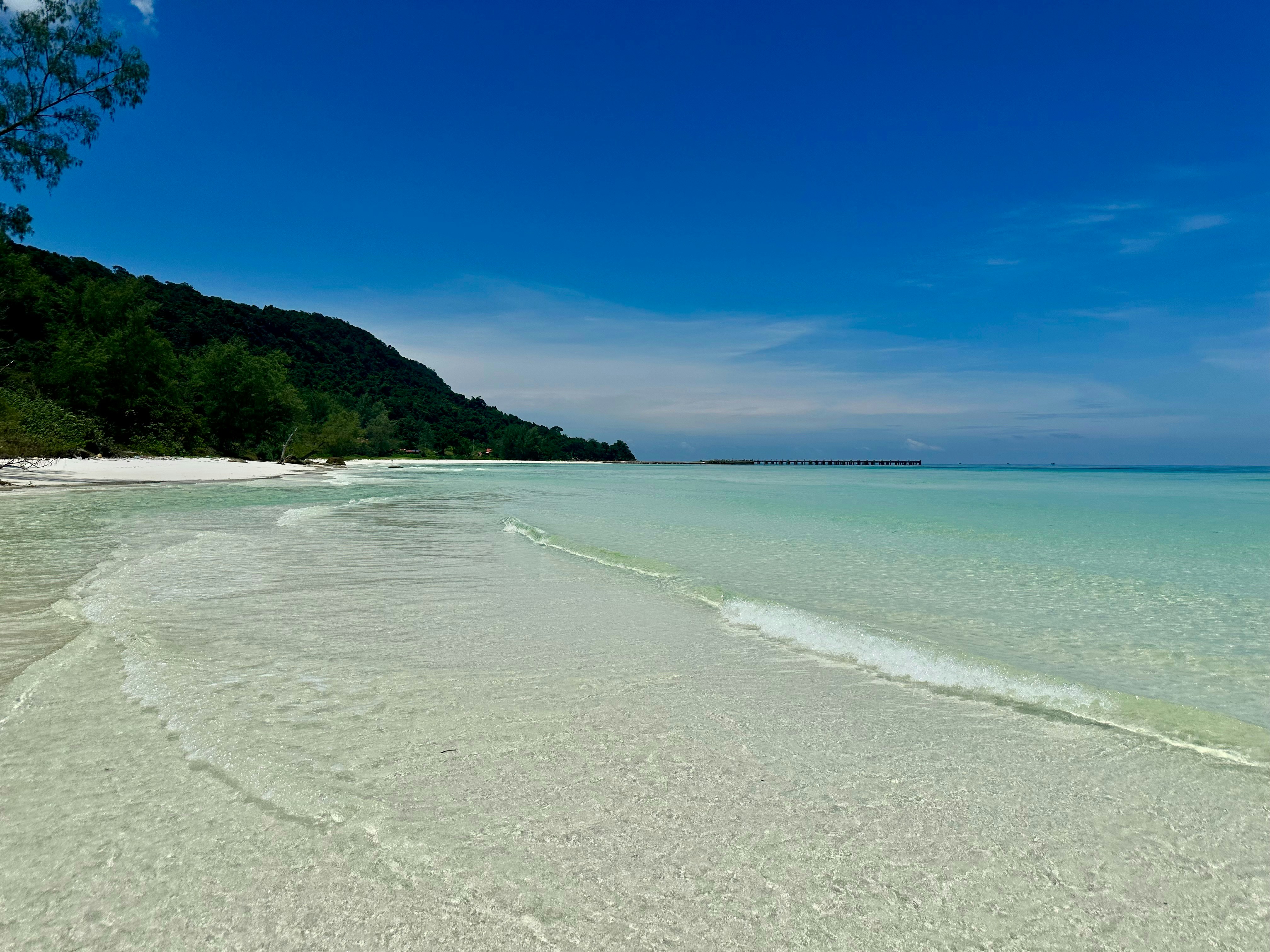 A sandy beach with clear blue water and a hill in the distance