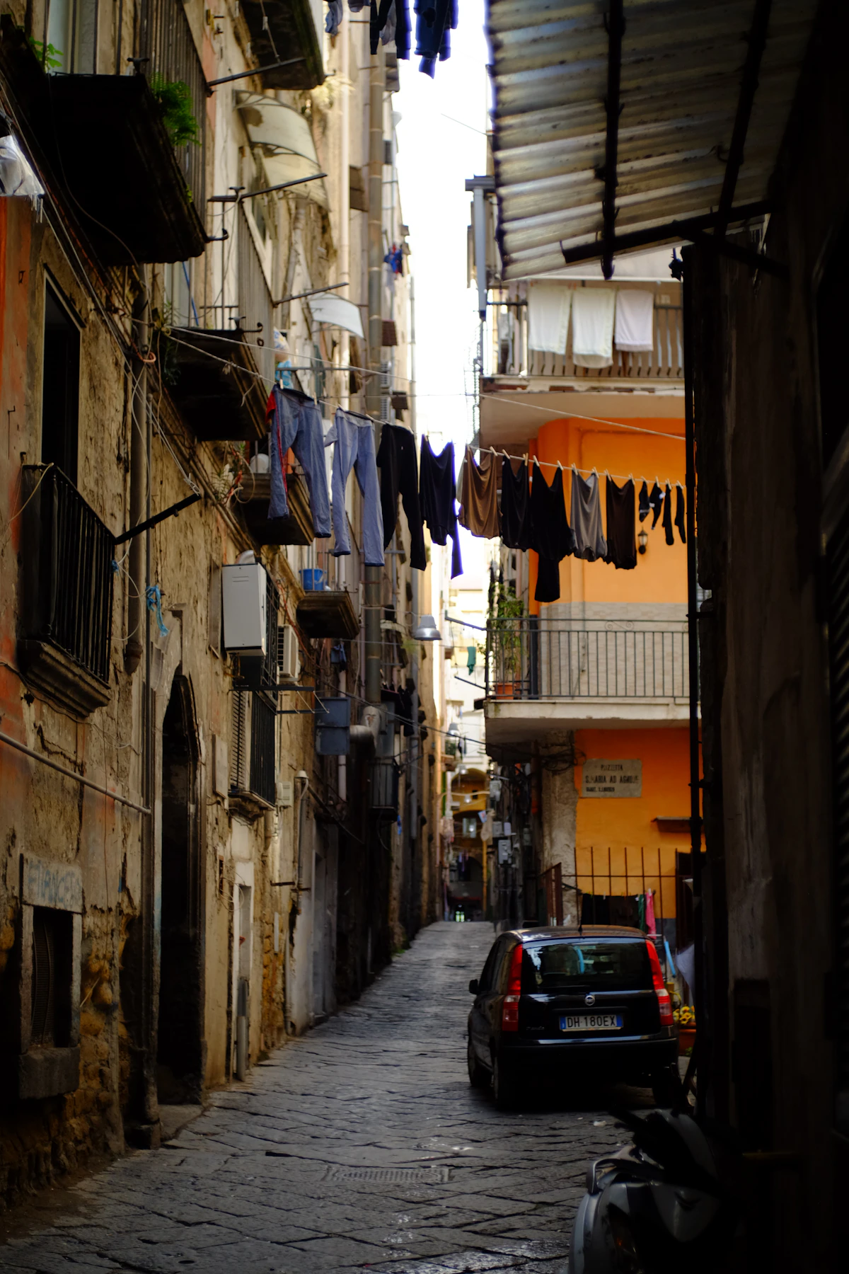 Laundry hanging above a narrow cobbled lane between lived-in buildings in Naples