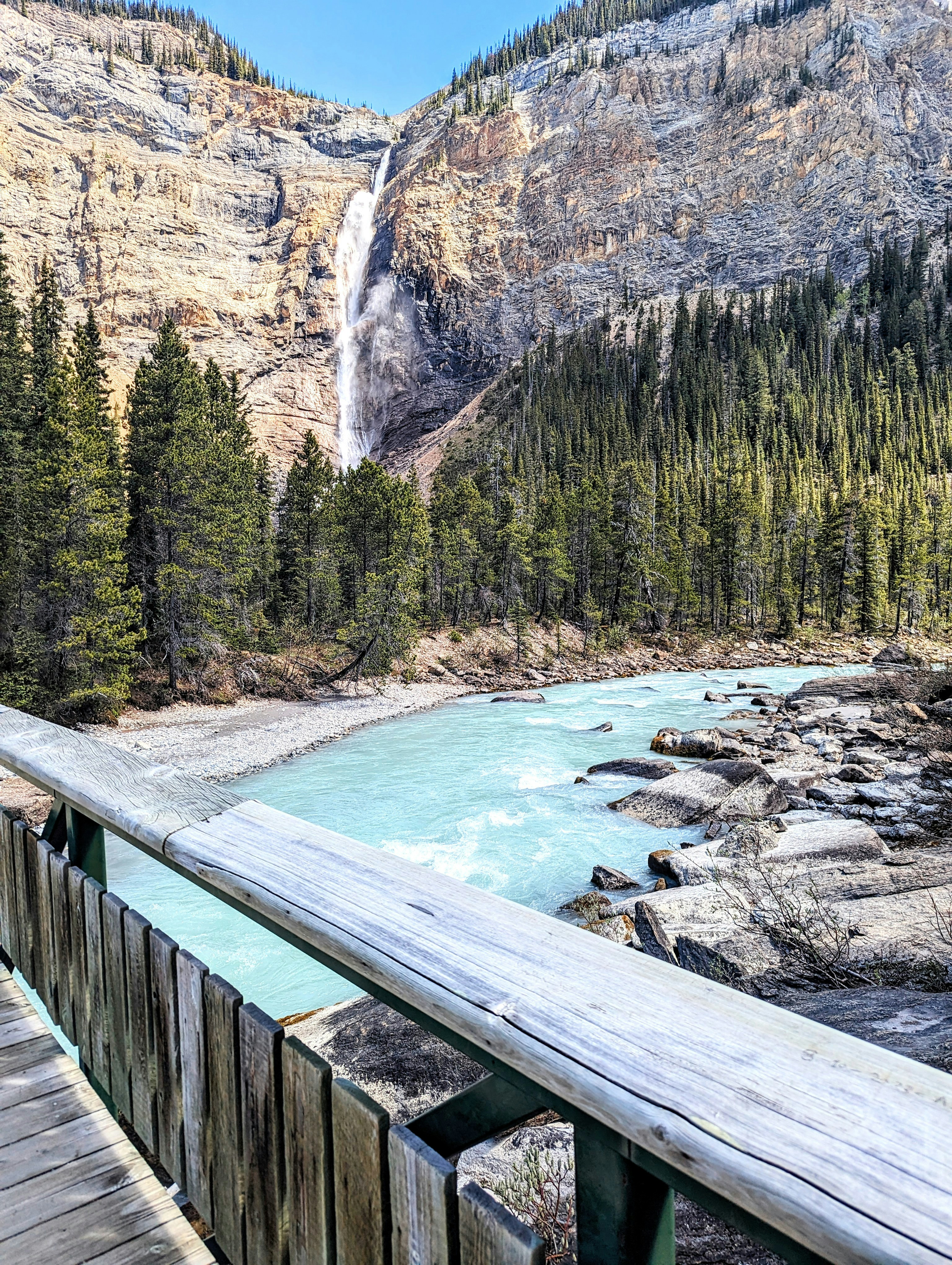 A wooden bridge over a river with a waterfall in the background