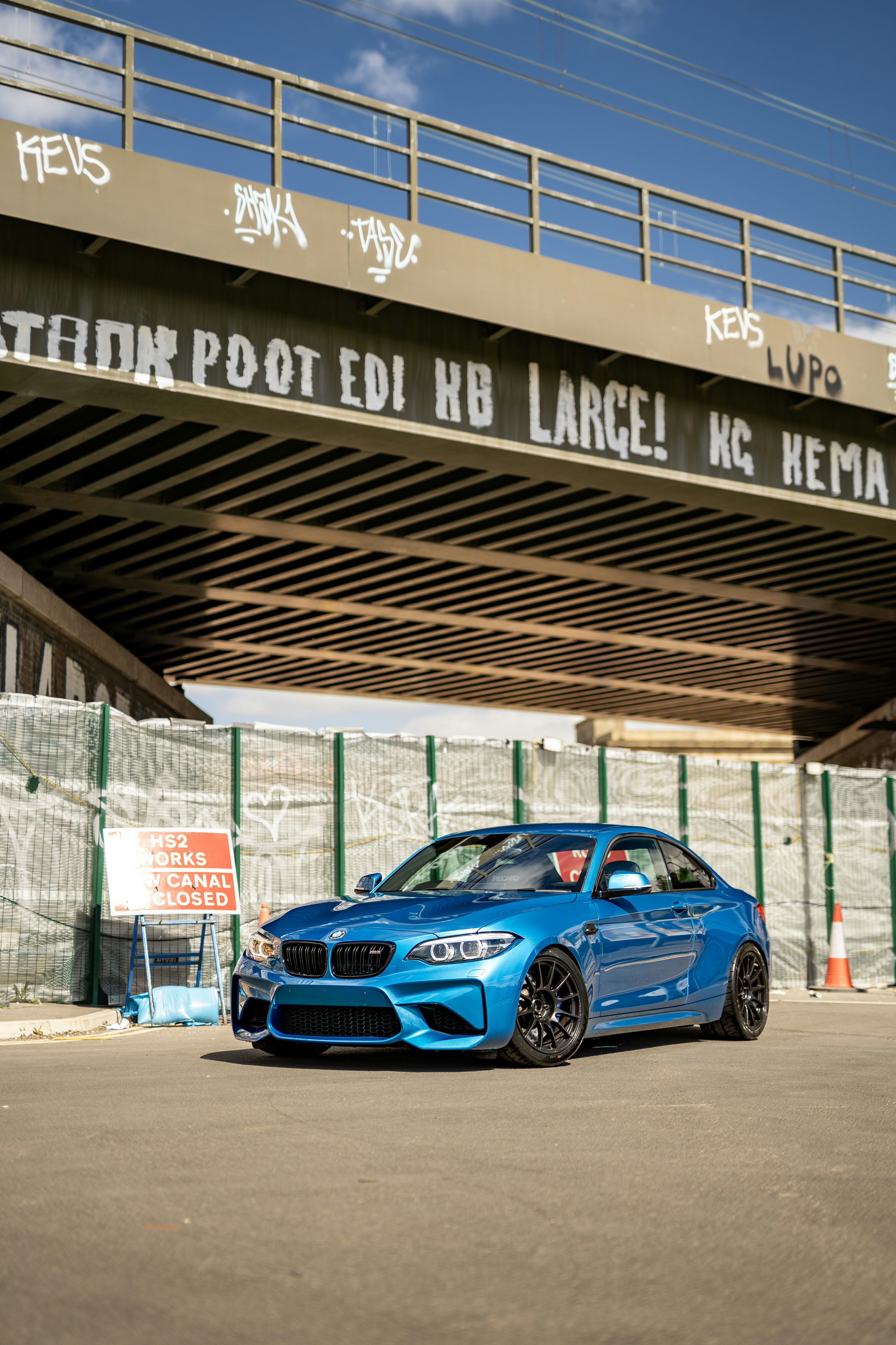A blue car is parked under a bridge