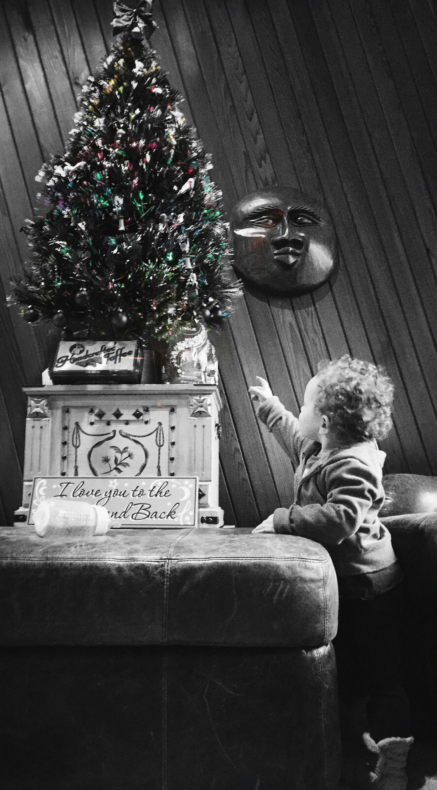 A little boy sitting on a couch next to a christmas tree