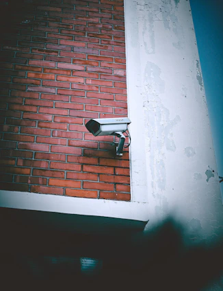 A security camera mounted to the side of a brick building