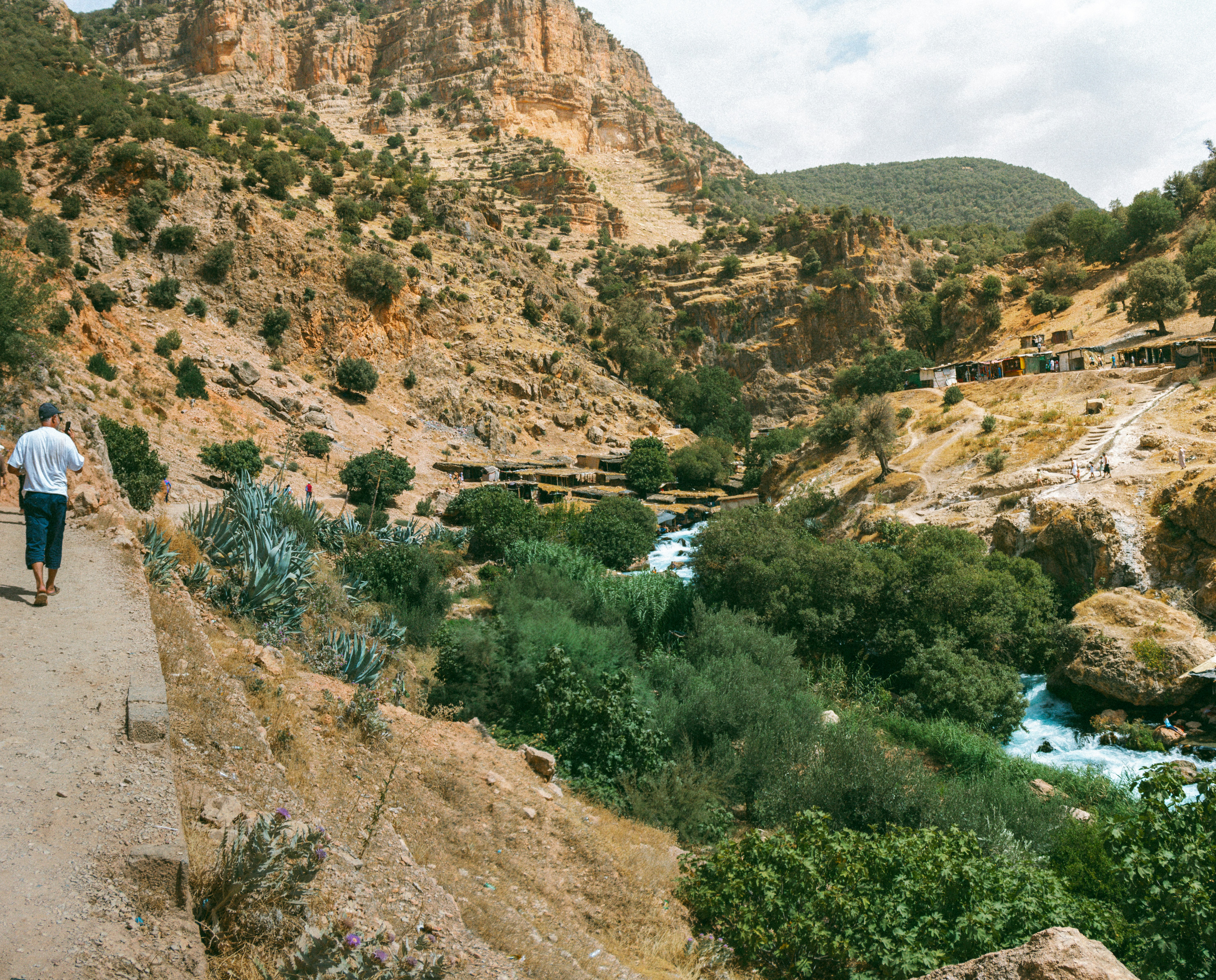 A man walking down a dirt road next to a river