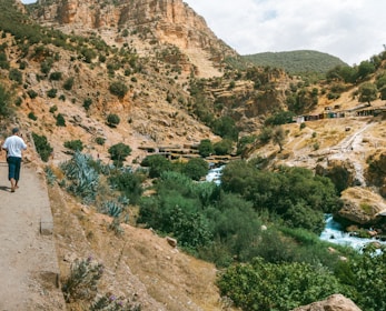 A man walking down a dirt road next to a river