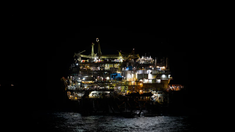 Oil rig platform illuminated at night in the ocean, representing global energy supply disruption