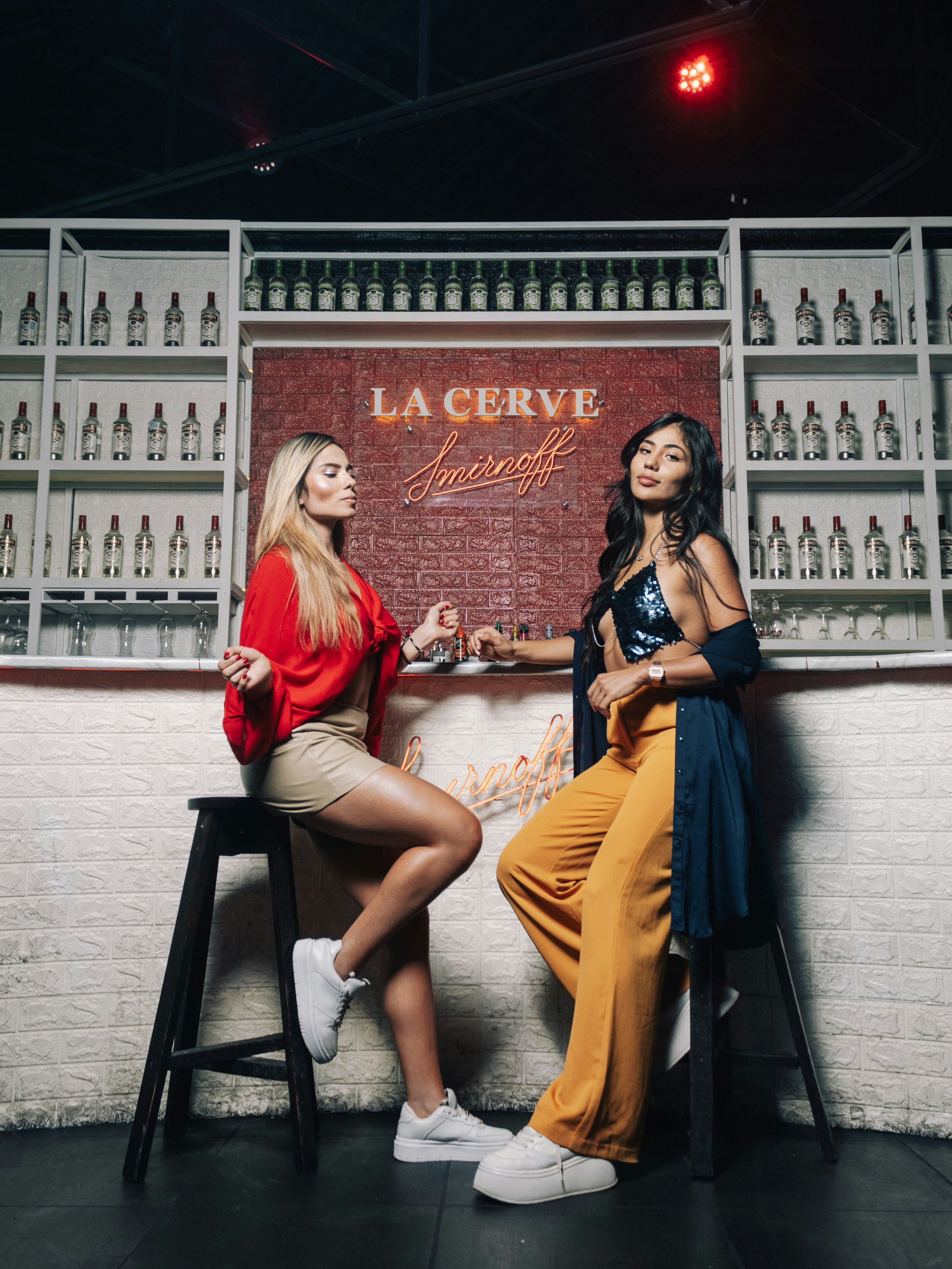 Two women sitting on stools in front of a bar
