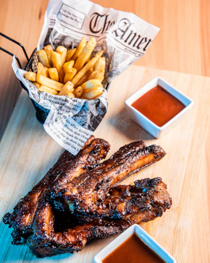 A wooden cutting board topped with ribs and french fries
