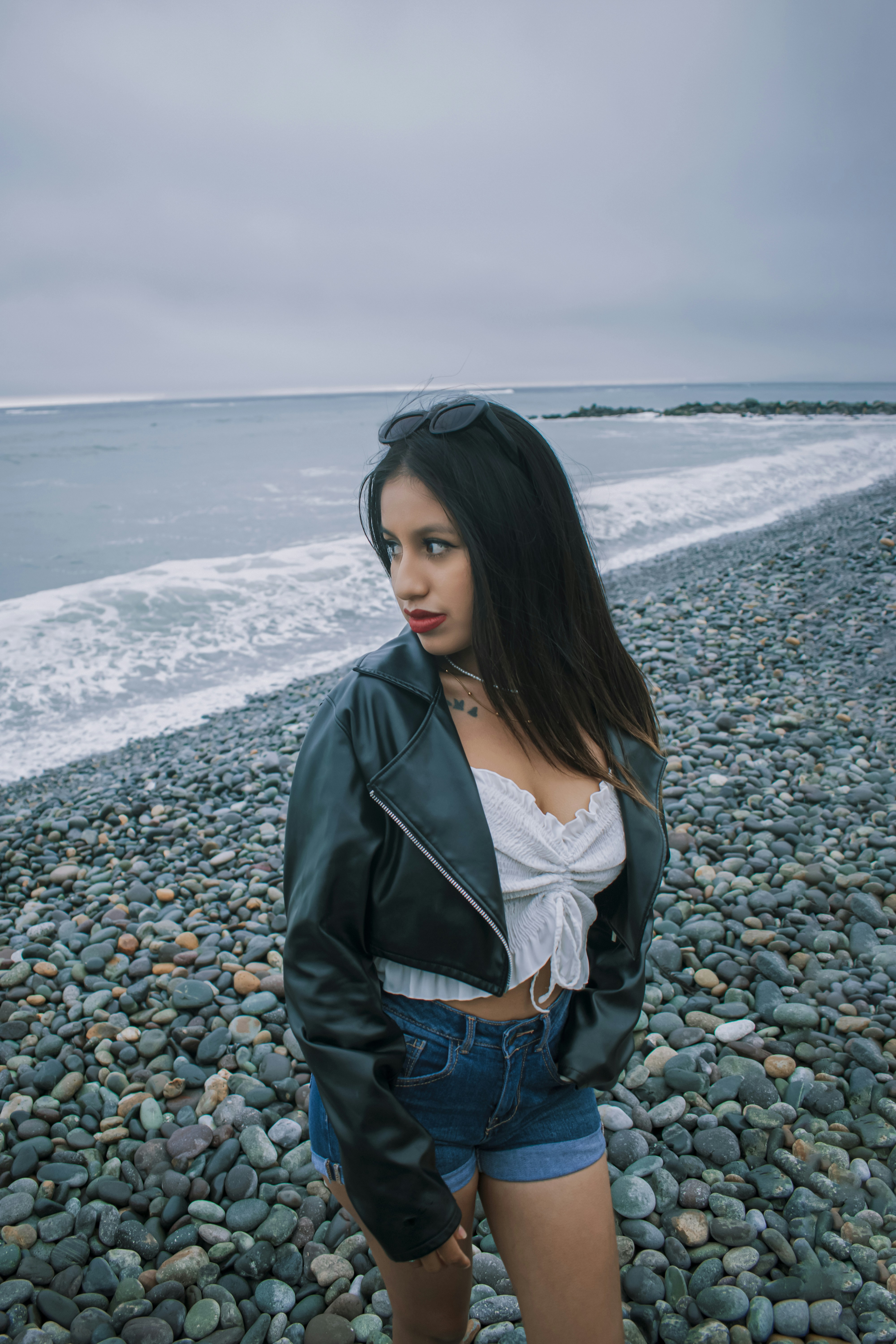 A woman standing on a rocky beach next to the ocean photo – Free Girl ...