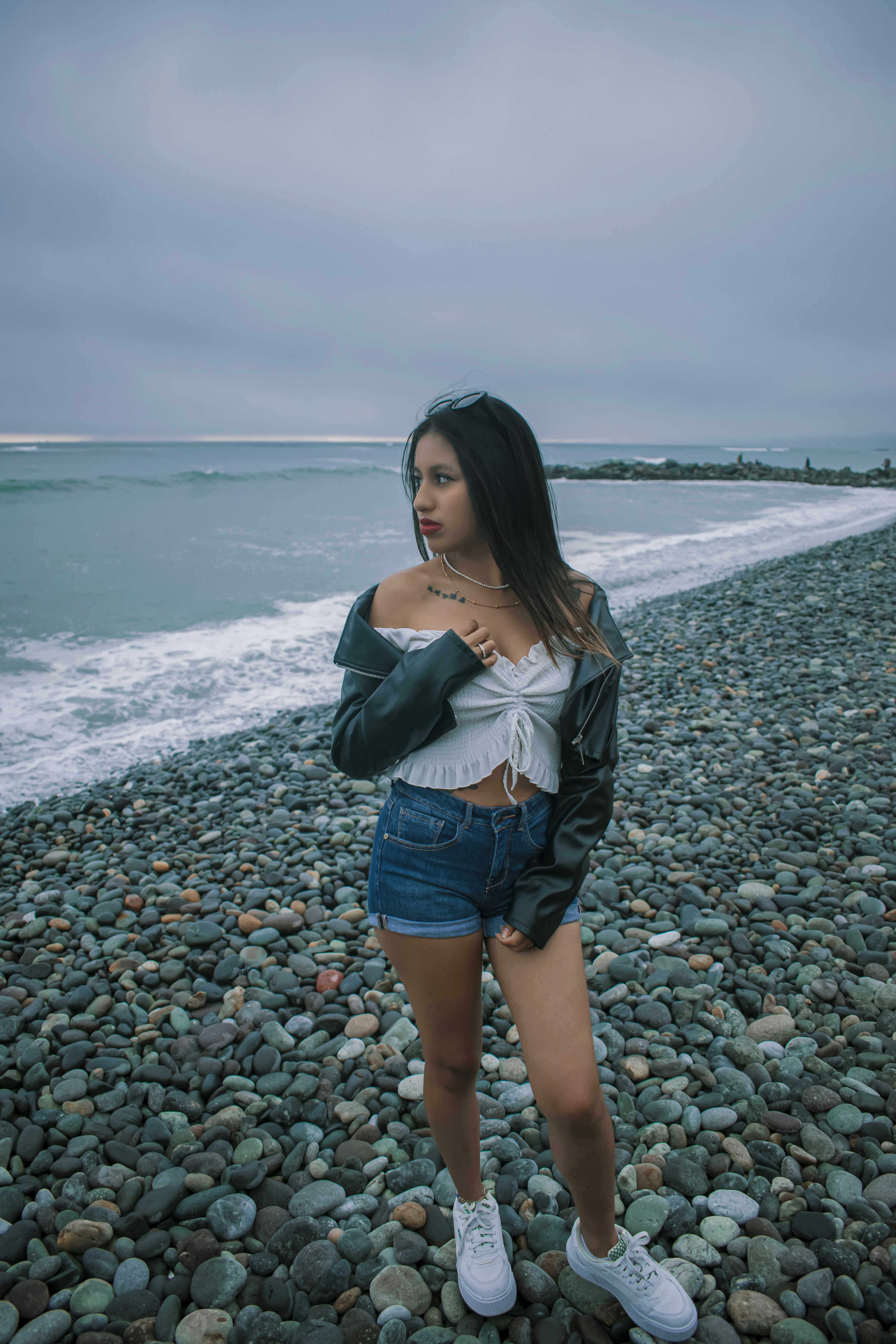 A woman standing on a rocky beach next to the ocean photo – Free Girl ...