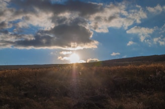 The sun is shining through the clouds over a field