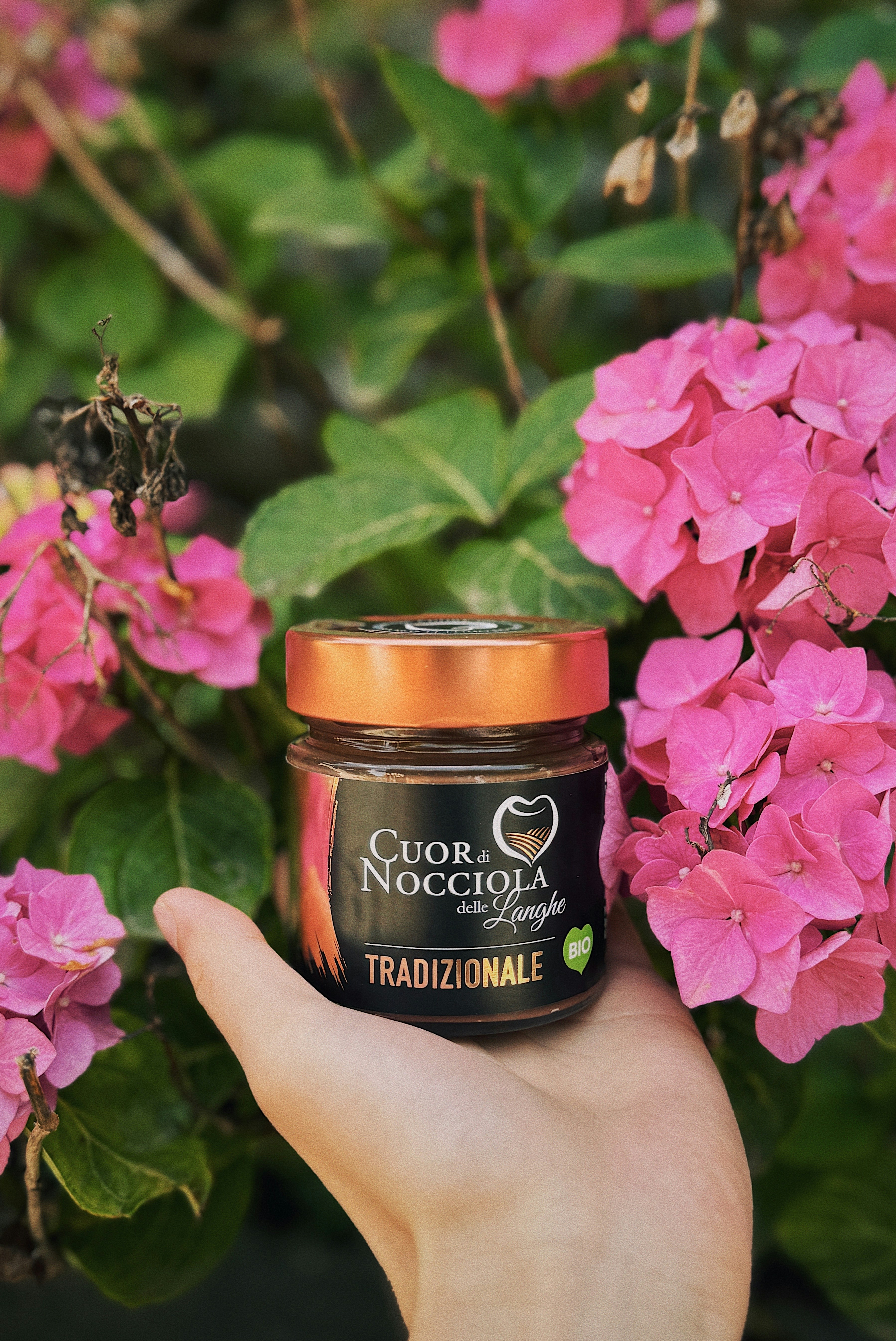 A hand holding a jar of nutella surrounded by pink flowers