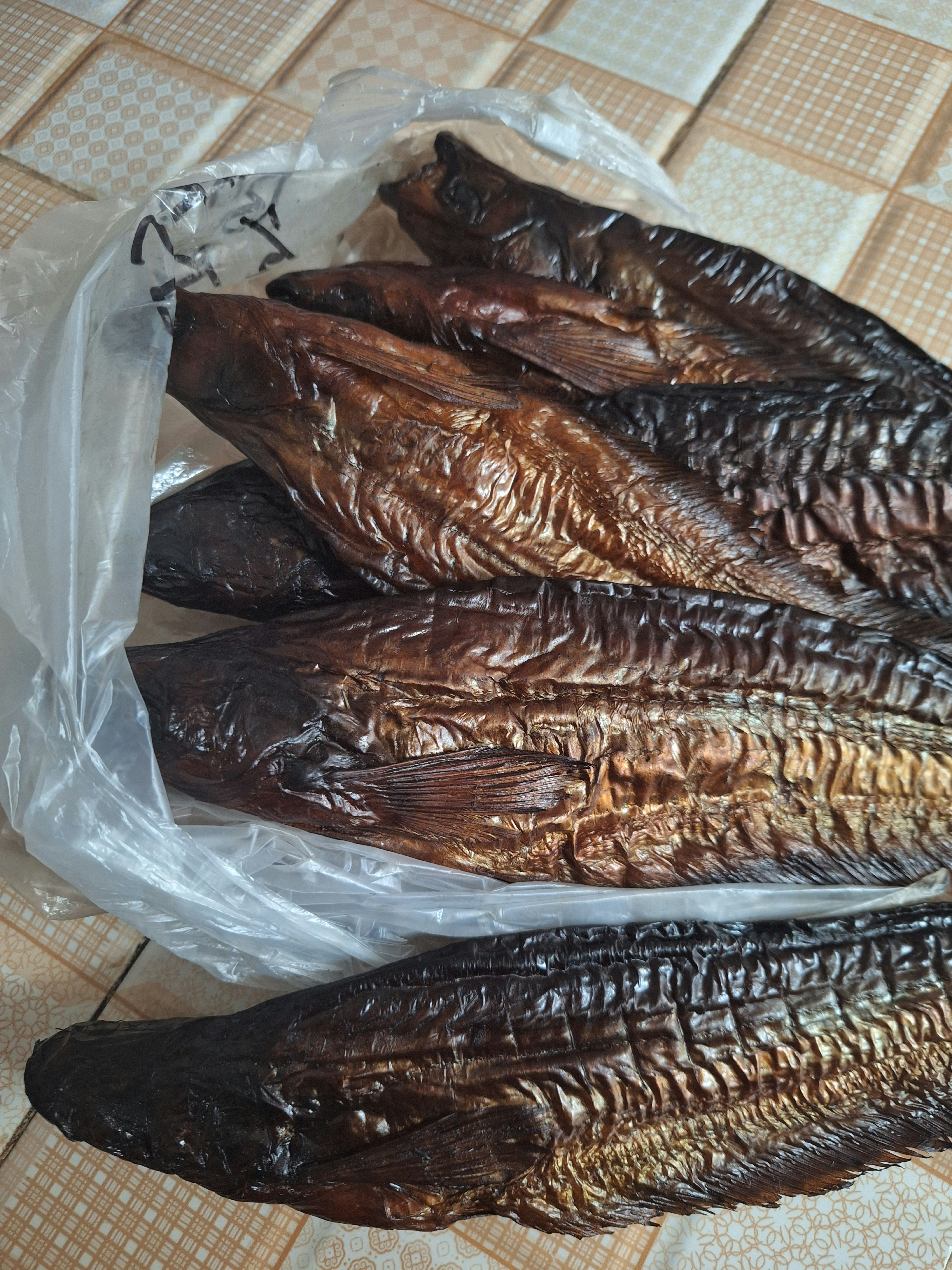 Dried smoked fish arranged on a rustic wooden surface, dark smoky skin, golden brown tones