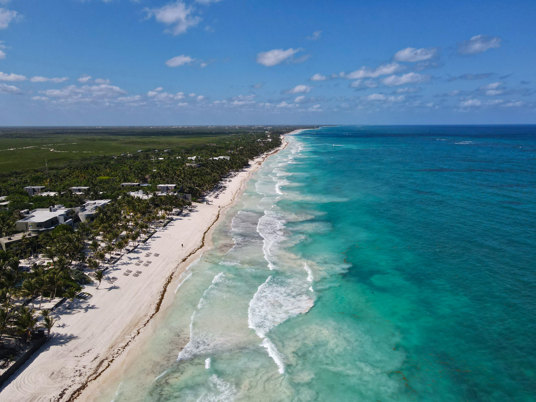 Aerial view of a calm reef-sheltered bay with a low-rise palm-lined shoreline, Riviera Maya, Mexico