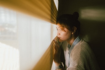 A woman looking out of a window while holding a curtain